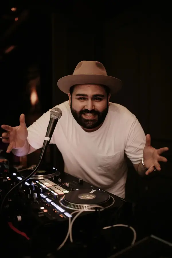 DJ SAM lachend mit Mikrofon hinter dem DJ-Pult