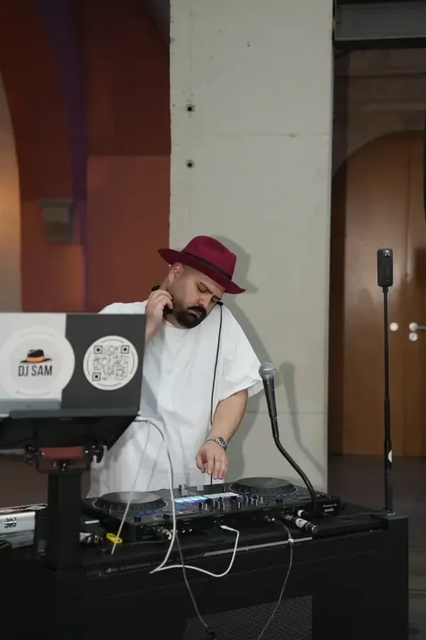 DJ SAM mit rotem Hut am DJ-Pult einer Hochzeit