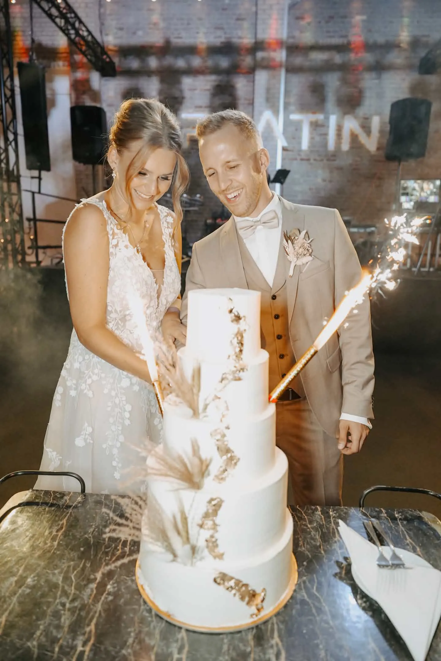 A. und K. schneiden lachend die f&uuml;nfst&ouml;ckige Hochzeitstorte mit Wunderkerzen an