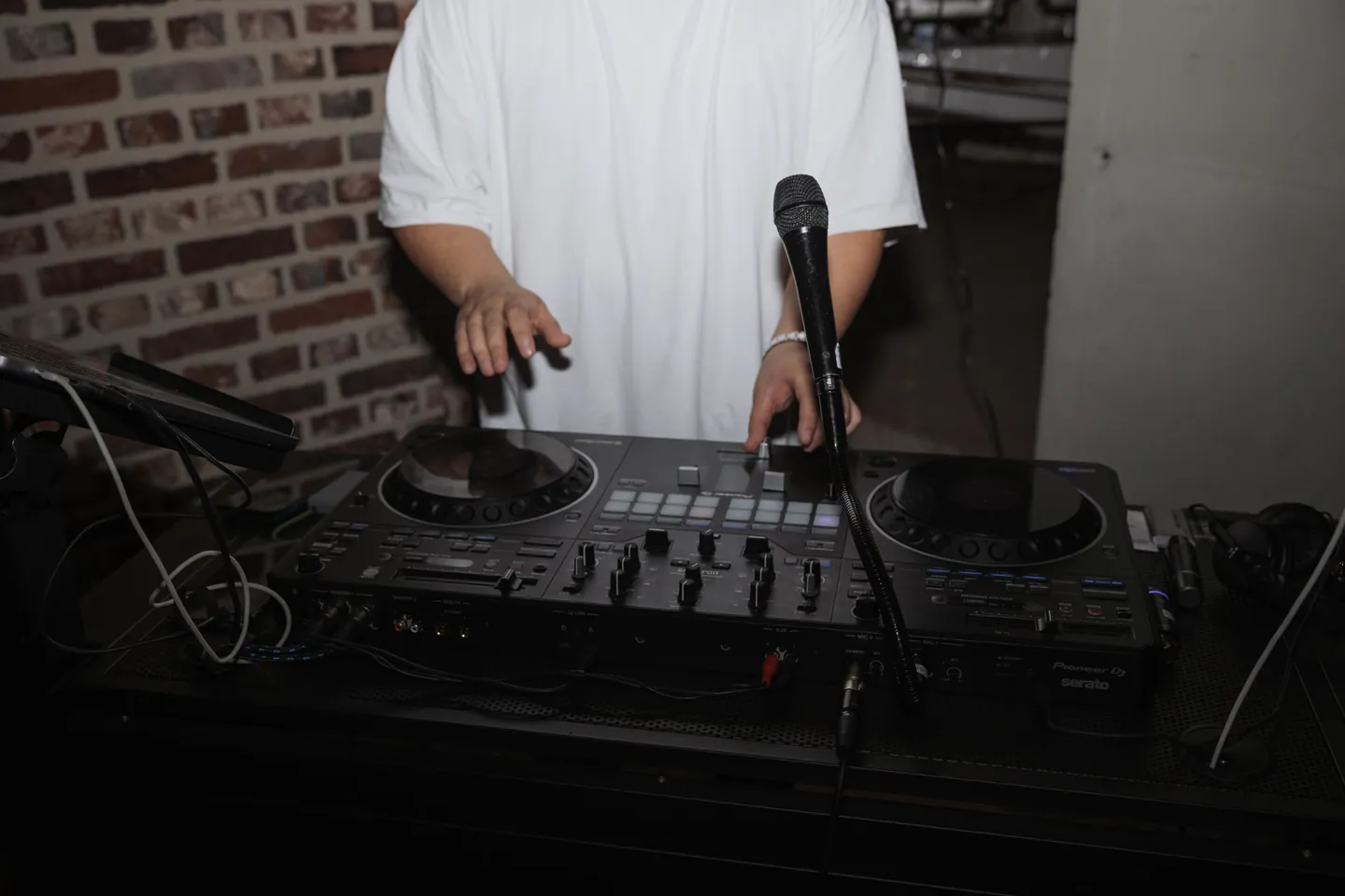 H&auml;nde von DJ SAM am Controller, Mikrofon am DJ-Pult vor einer Backsteinwand im Schloss Horst