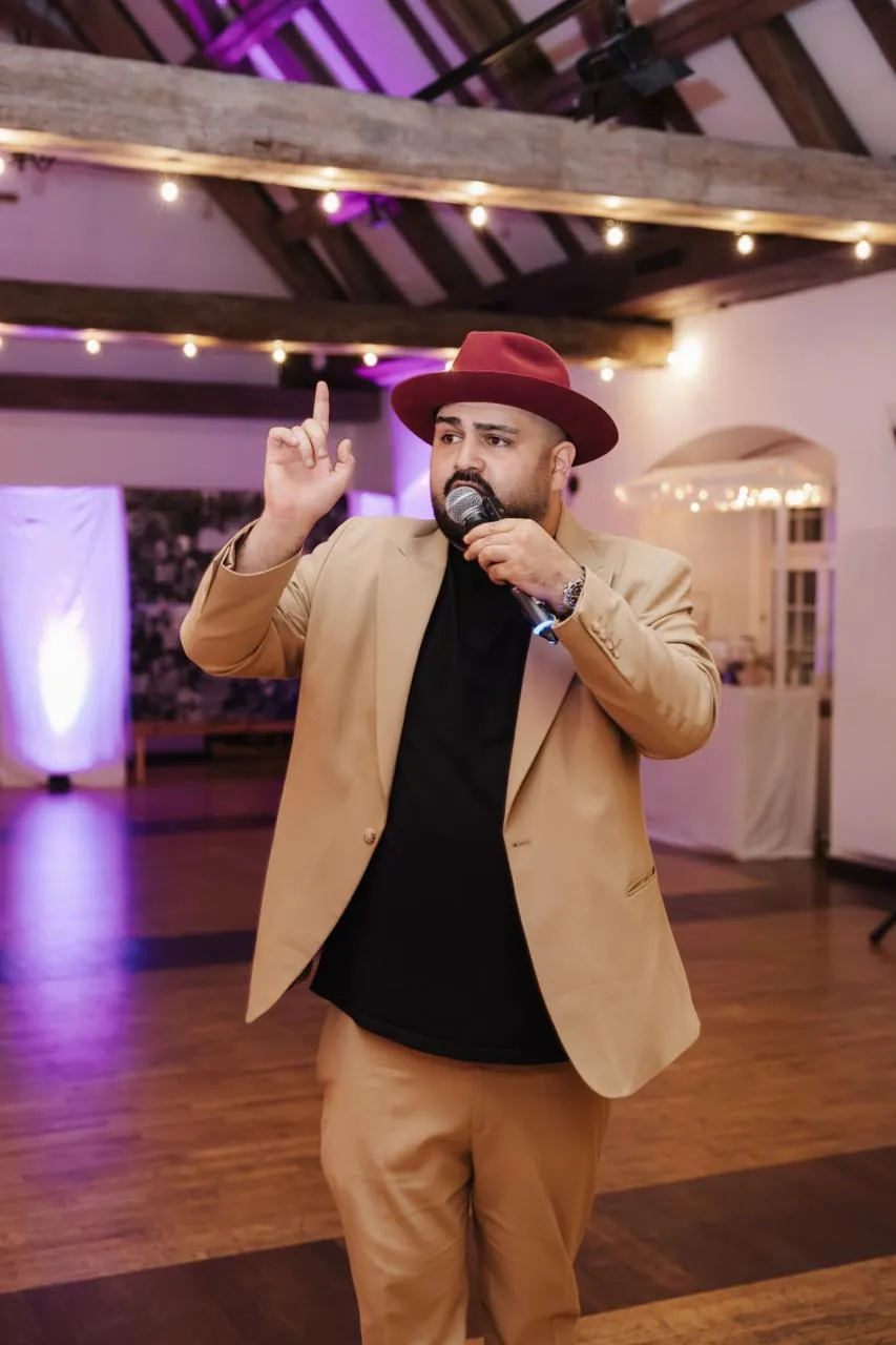 DJ SAM mit Mikrofon bei der Moderation in einem festlich beleuchteten Saal